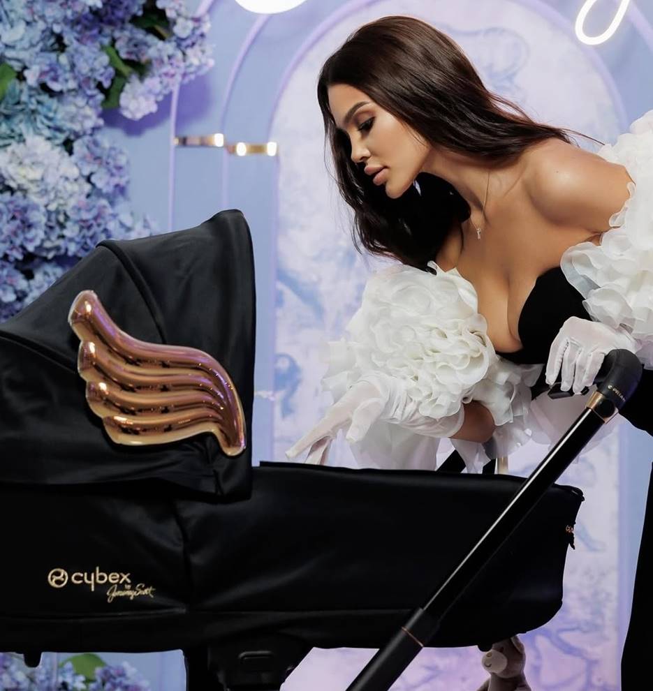Kobieta w eleganckiej sukni pochyla się nad wózkiem Cybex Priam Wings by Jeremy Scott – luksusowy wózek w balowej oprawie.